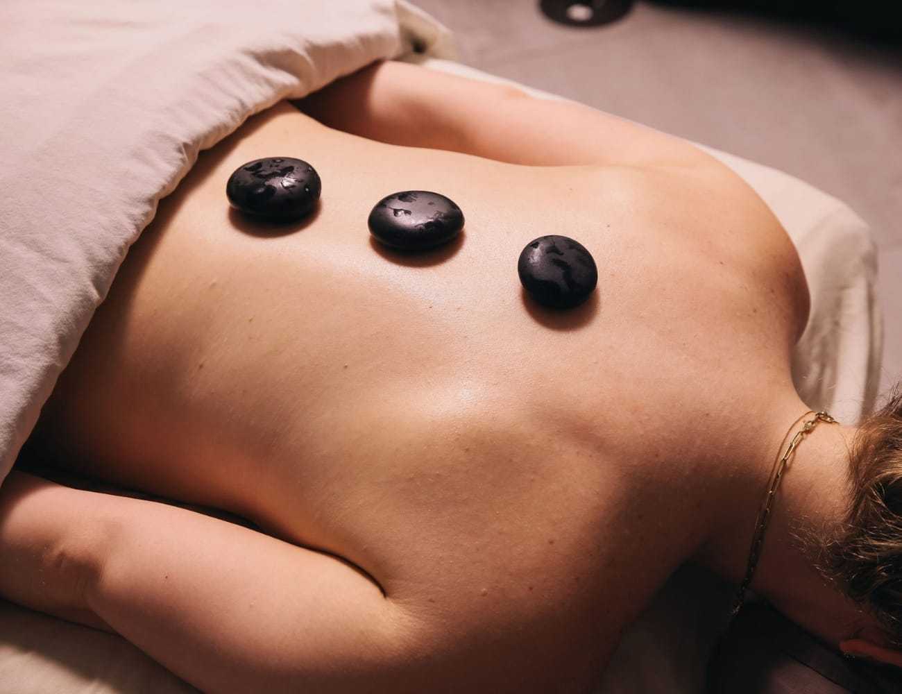 Person receiving a hot stone massage therapy on their back for relaxation.