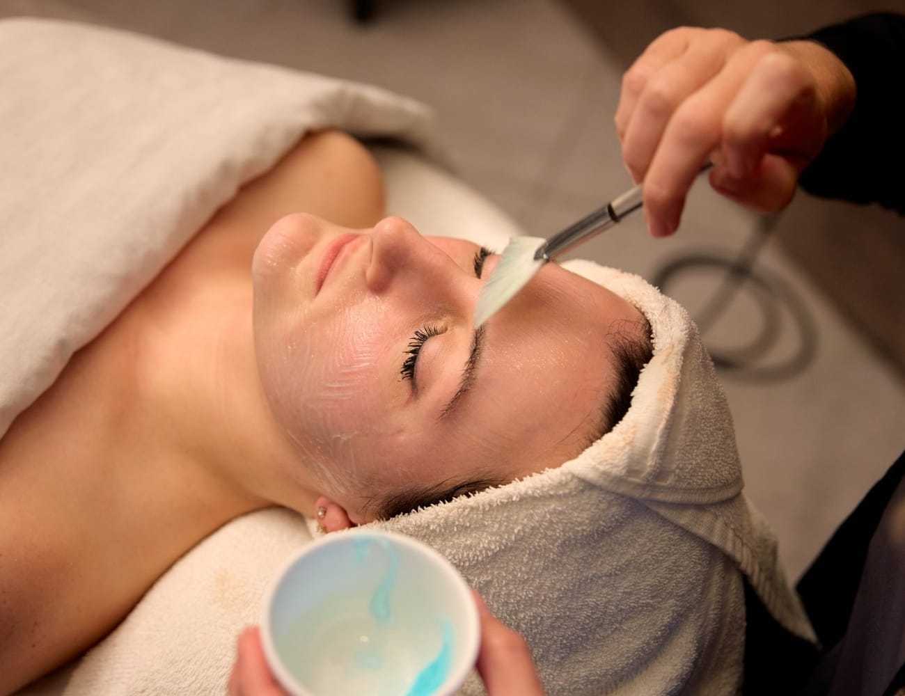 Person receiving a facial treatment at a spa, with brush applying a mask.